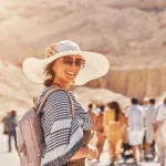 Smiling traveler in a sun hat at the Valley of the Kings in Egypt, surrounded by a group of Discovery Tours Egypt tourists, exploring ancient wonders.