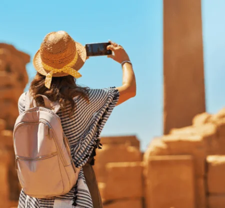 Traveler, traveling with Discovery Tours Egypt, taking a photo of ancient ruins in Egypt with a smartphone, wearing a straw hat, capturing Egypt’s rich history.