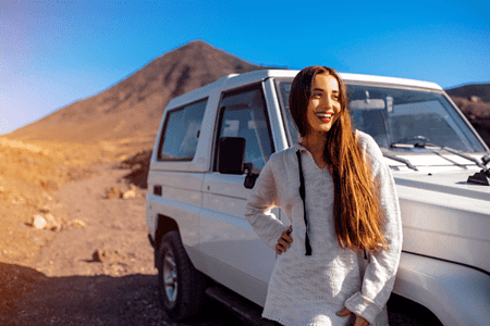 Smiling traveler standing next to a 4x4 vehicle in the desert of Egypt with mountains in the background.