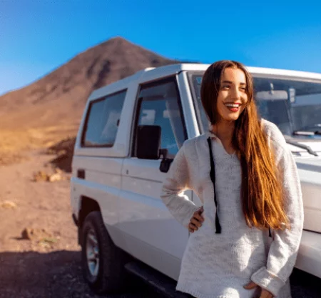 Smiling traveler standing next to a 4x4 vehicle in the desert of Egypt with mountains in the background.
