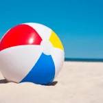 Colorful beach ball resting on sandy beach in Egypt with ocean and clear blue sky in the background.