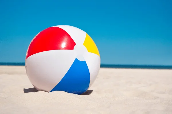 Colorful beach ball resting on sandy beach in Egypt with ocean and clear blue sky in the background.